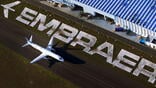 An Embraer jet taxis across a tarmac that features the Embraer company logo