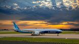 A Boeing 777-9 sits on a runway at sunset.