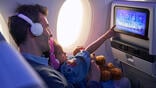 parent and child sitting on aircraft with inflight entertainment screen lit